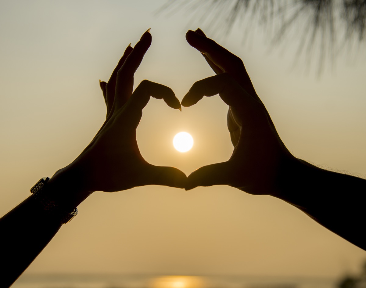Hands forming a heart around the setting sun